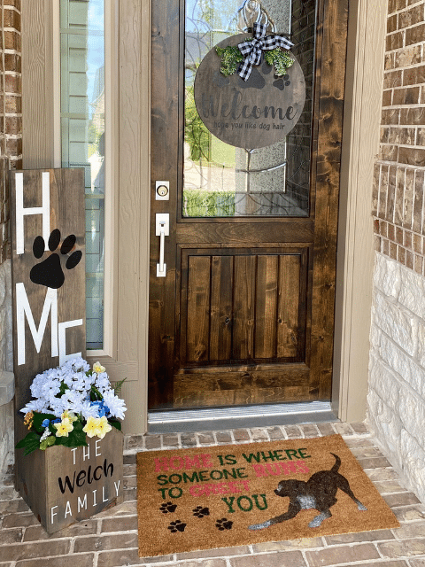 Front porch decorated with handmade wooden signs, welcome wreath, and custom doormat and a planter box.
