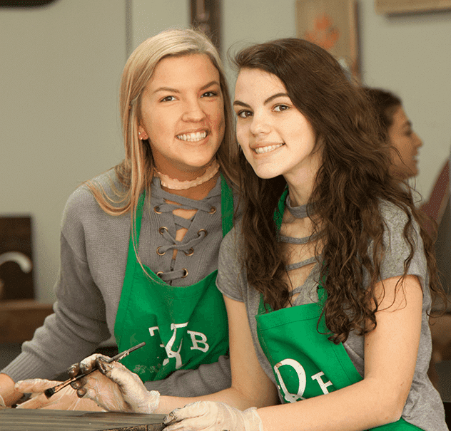 Two participants wearing aprons working together on a hands-on DIY crafting project.