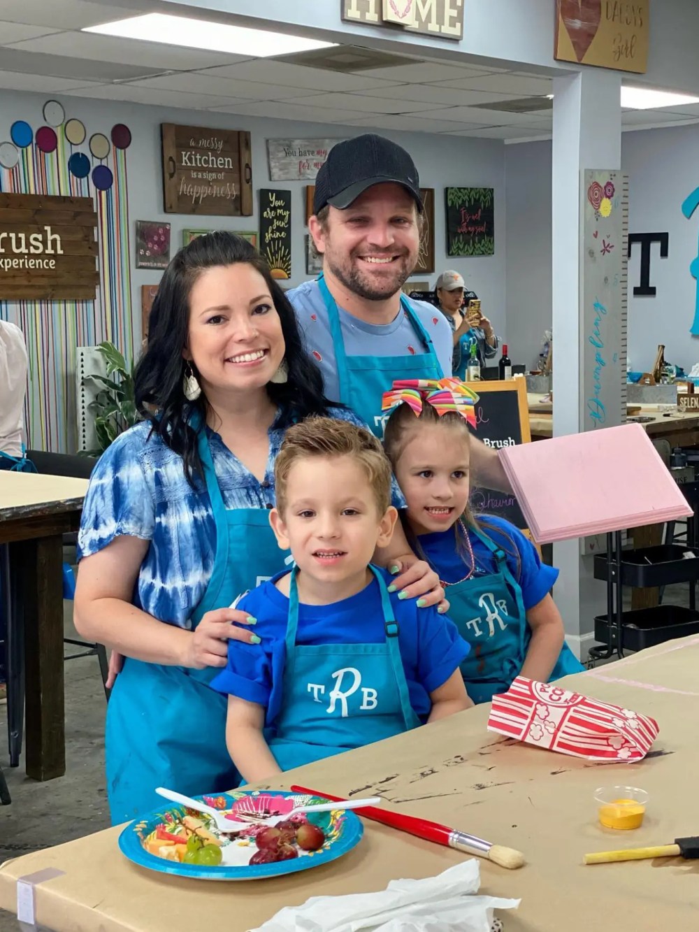 Family posing together in matching aprons at a wood sign painting event.