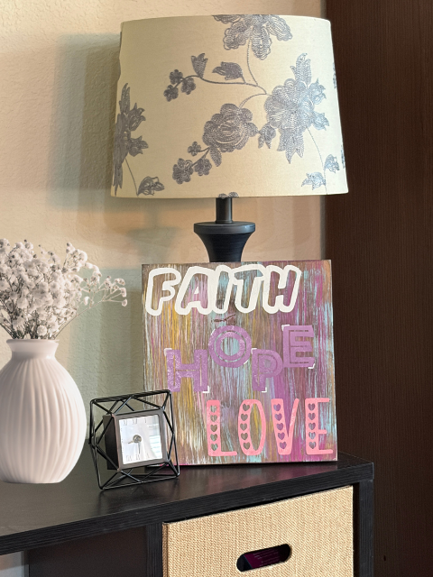 Lamp, vase, and decor sign with 'Faith Hope Love' on table.