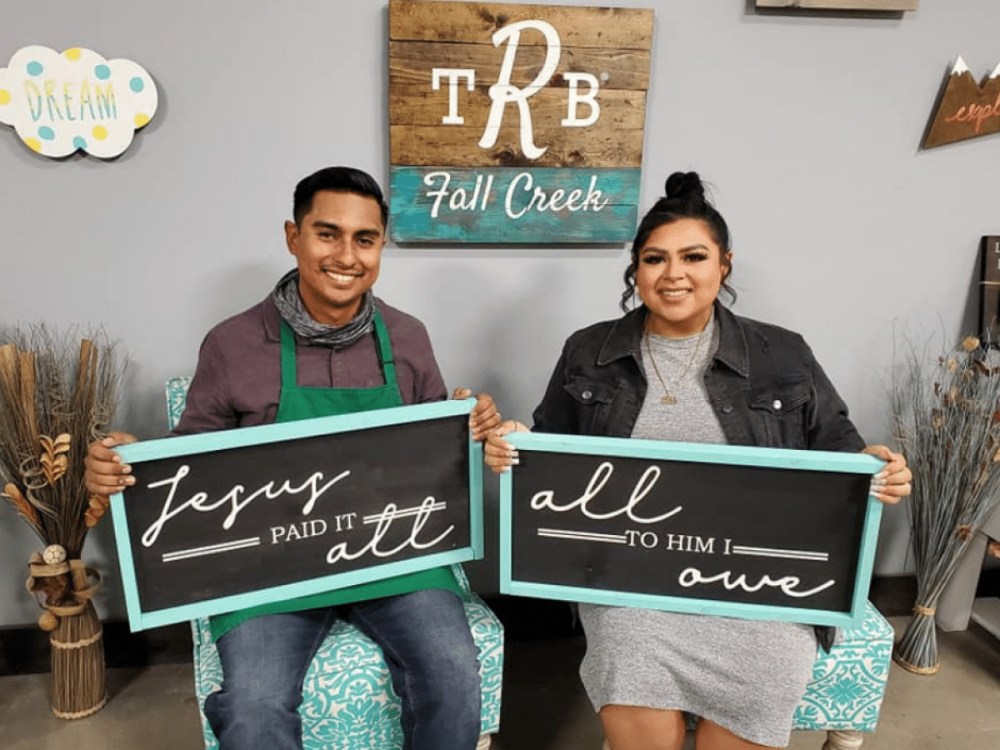 Couple displaying matching handmade wooden signs after a DIY crafting class at The Rustic Brush.