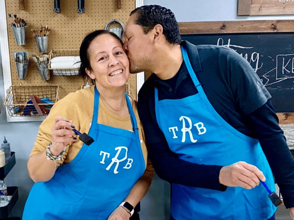 Couple wearing workshop aprons while painting together at The Rustic Brush.