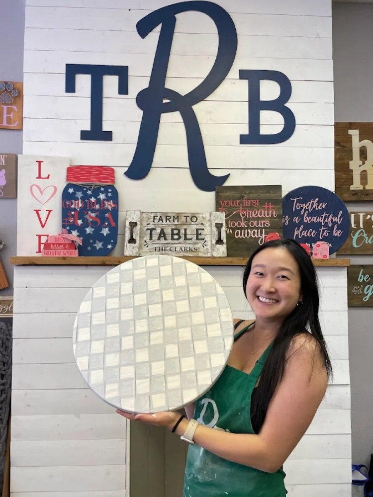 Participant holding a handcrafted round wood decor piece after a paint and sip DIY workshop.