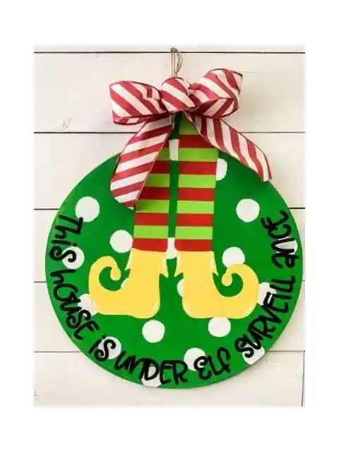 A green "Elf Surveillance" round wooden door sign.