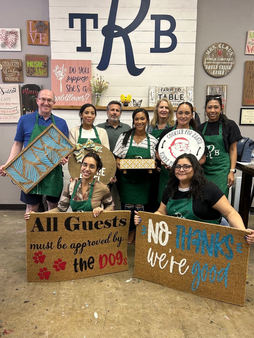 A group in green aprons holding custom signs and doormats at The Rustic Brush.