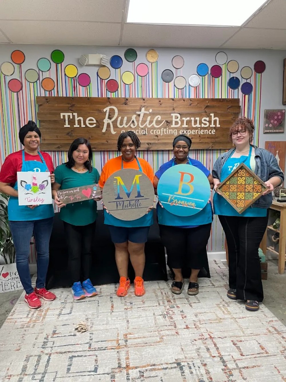 Five participants displaying personalized wooden signs they created during a DIY workshop at The Rustic Brush.