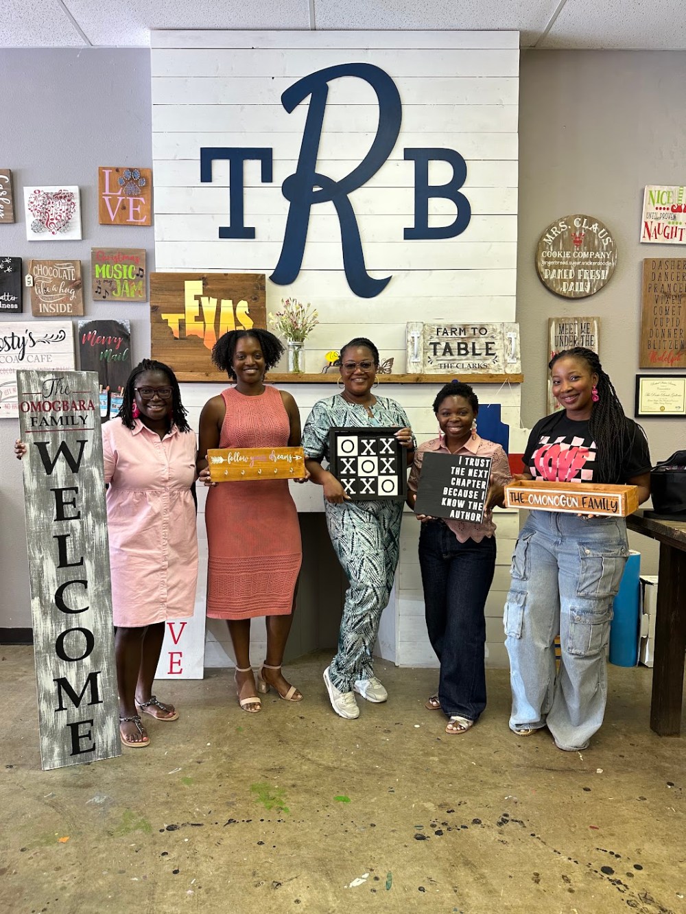 Five women holding custom wooden craft signs at a studio.
