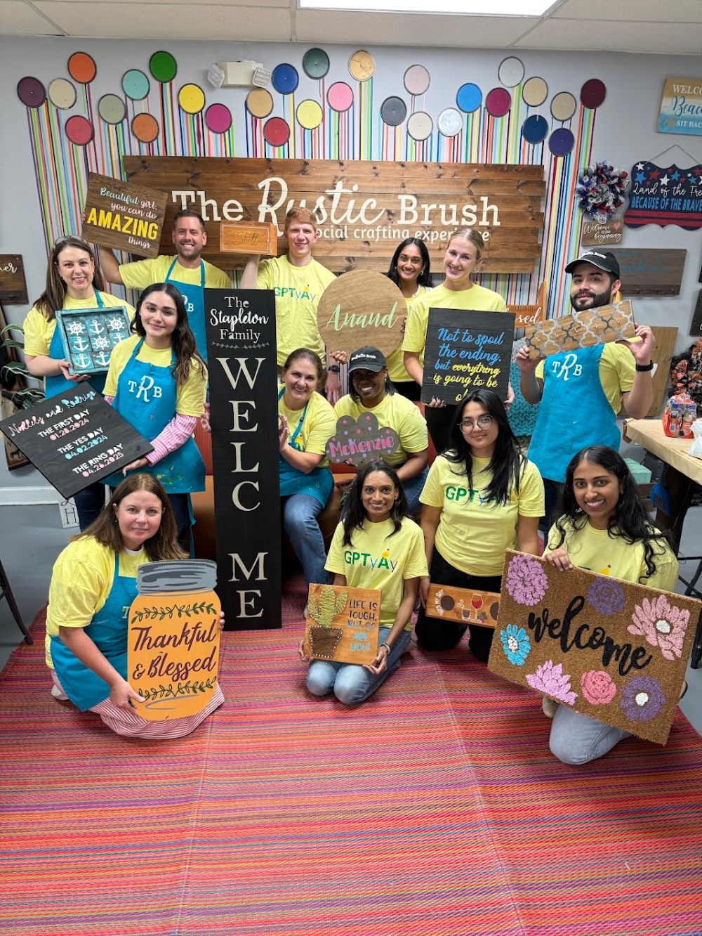 Group posing with personalized wood signs and home décor projects created during a workshop at The Rustic Brush.