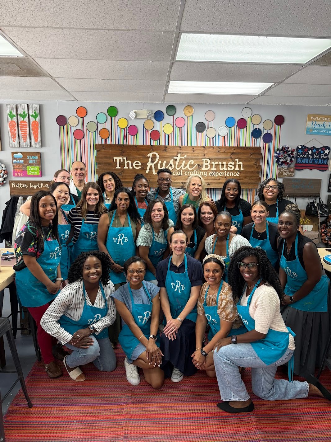 Large group wearing blue crafting aprons posing together after a creative workshop at The Rustic Brush.