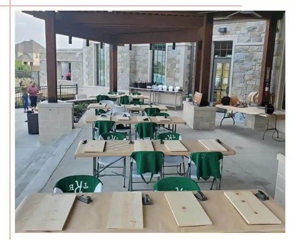 Outdoor DIY workshop setup with wooden project boards arranged on tables under a covered pavilion, ready for a group crafting event.