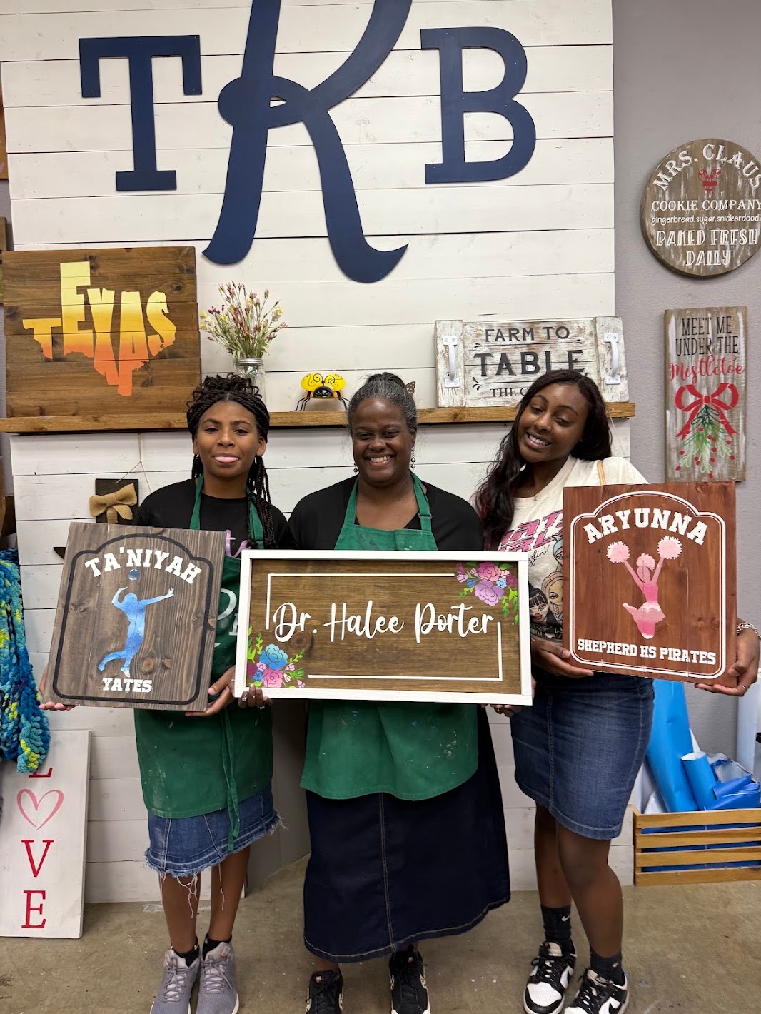 Participants holding their custom wooden signs after completing a DIY painting and woodworking workshop at The Rustic Brush.