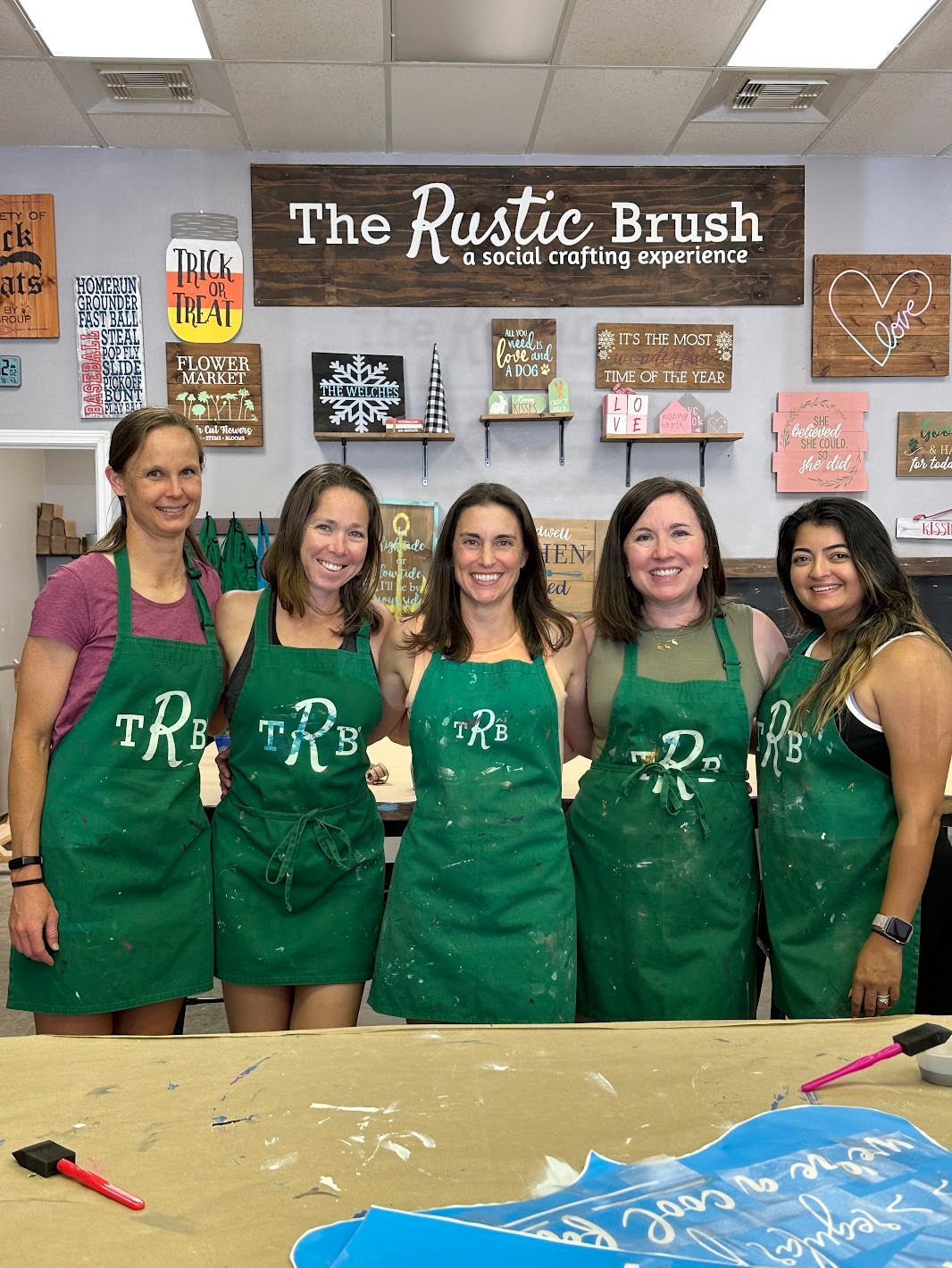 Participants wearing green aprons posing together during a DIY crafting workshop at The Rustic Brush.